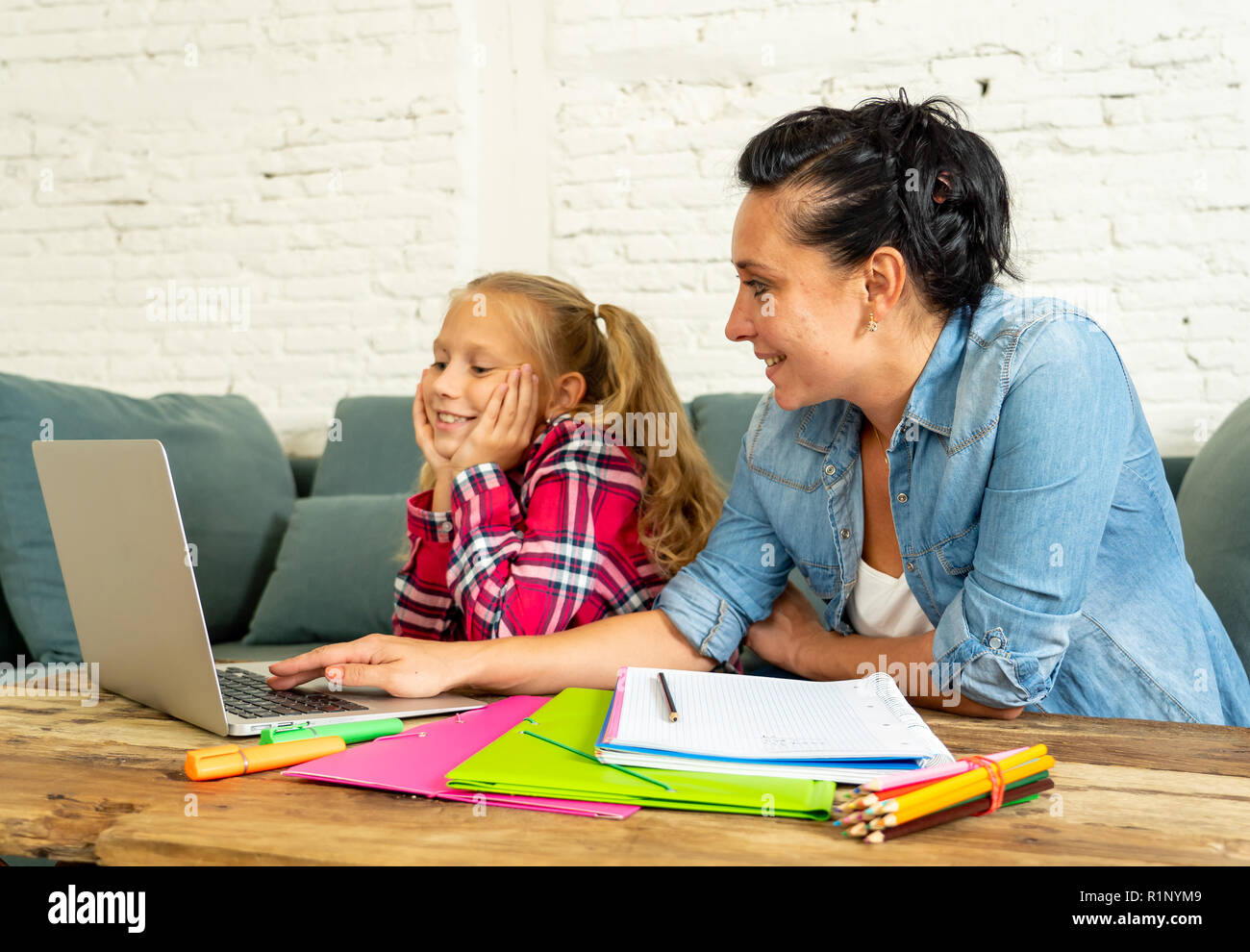 Mère Fille d'aider les jeunes à faire leurs devoirs avec ordinateur portable et des livres d'école assis sur le canapé à la maison de la parentalité et de l'éducation à domicile concept Banque D'Images
