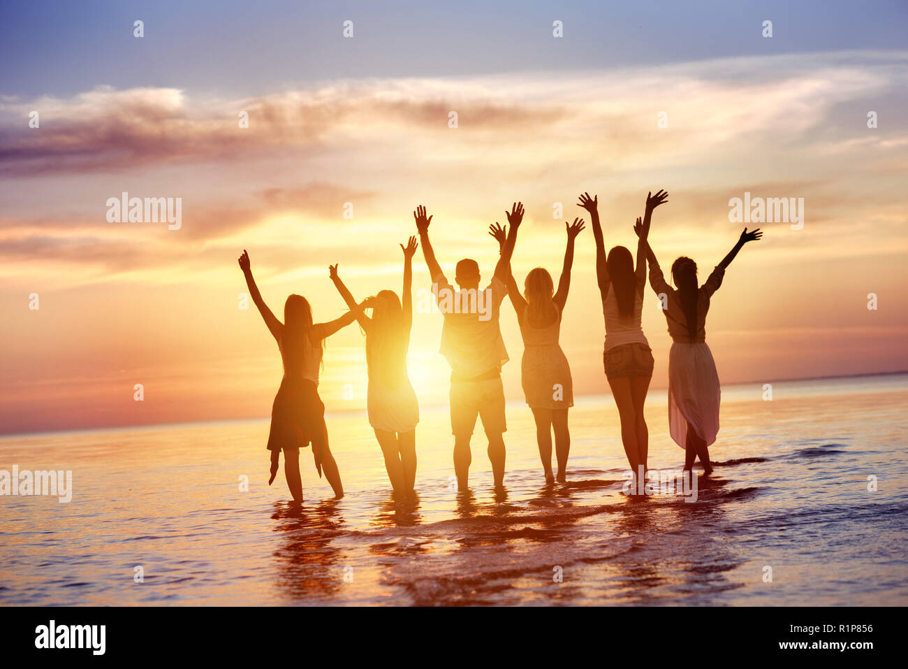 Groupe de six amis heureux ressemble au coucher du soleil sur l'eau Banque D'Images