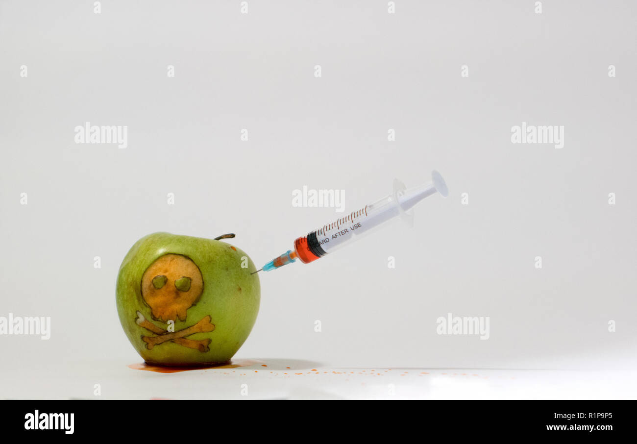 Seringue insérée dans une pomme verte avec un crâne gravé, photo représentative de l'utilisation des substances OGM dans les aliments, les légumes et les fruits Banque D'Images