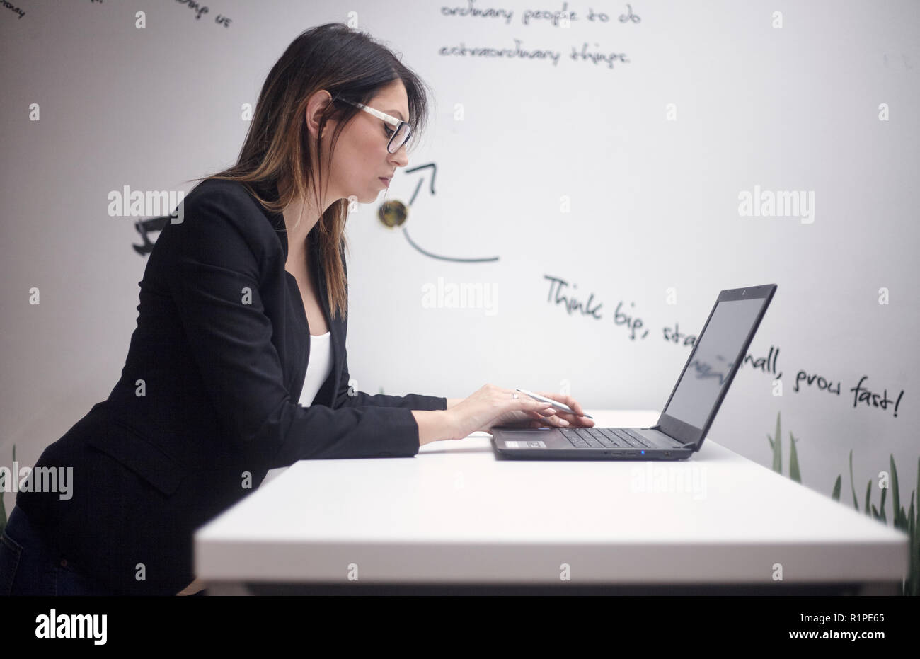Une jeune femme sérieuse, de 30 à 39 ans, vue latérale, haut du corps tourné. working on laptop. mur avec des citations créatives derrière. Banque D'Images