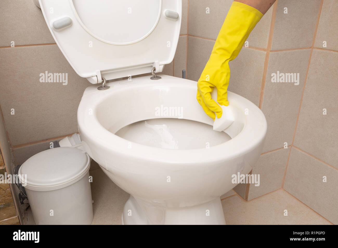 Personne portant des gants en latex jaune porcelaine de nettoyage de la cuvette des toilettes avec éponge Banque D'Images