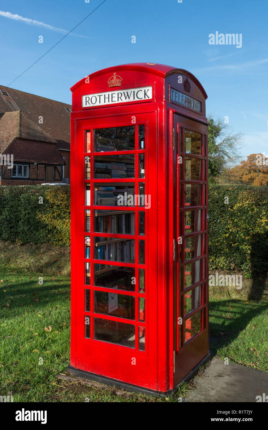 Téléphone rouge à l'ancienne fort ou d'un kiosque sur la rue près de la salle des fêtes dans le village de Rotherwick dans le Hampshire, au Royaume-Uni, maintenant utilisé comme une bibliothèque Banque D'Images