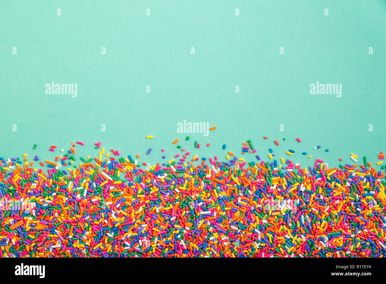 Mise à plat de bonbons colorés saupoudre le long du bord inférieur d'un fond vert pastel Banque D'Images