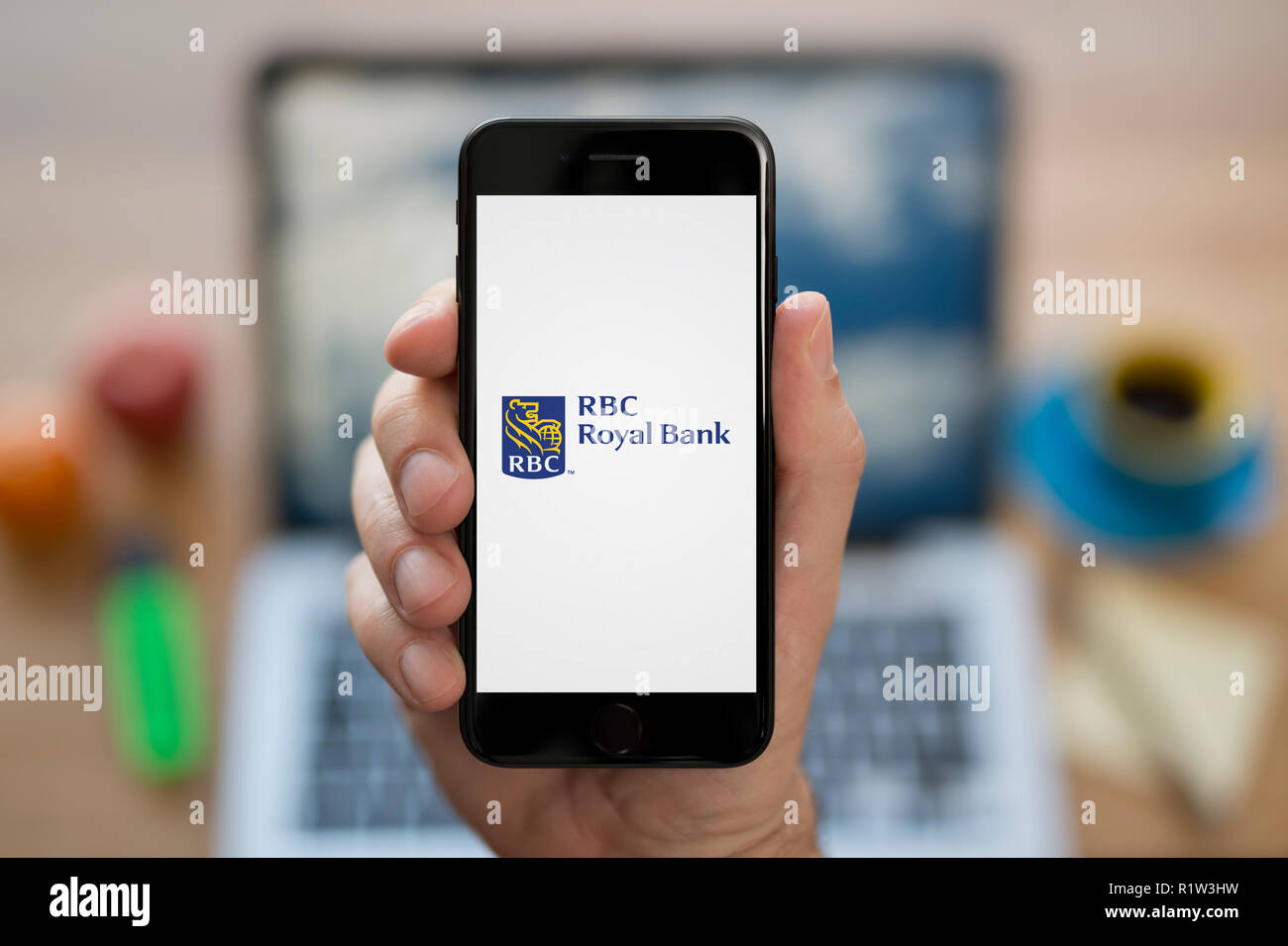 Un homme se penche sur son iPhone qui affiche le logo de RBC Banque Royale, en restant assis devant son ordinateur 24 (usage éditorial uniquement). Banque D'Images