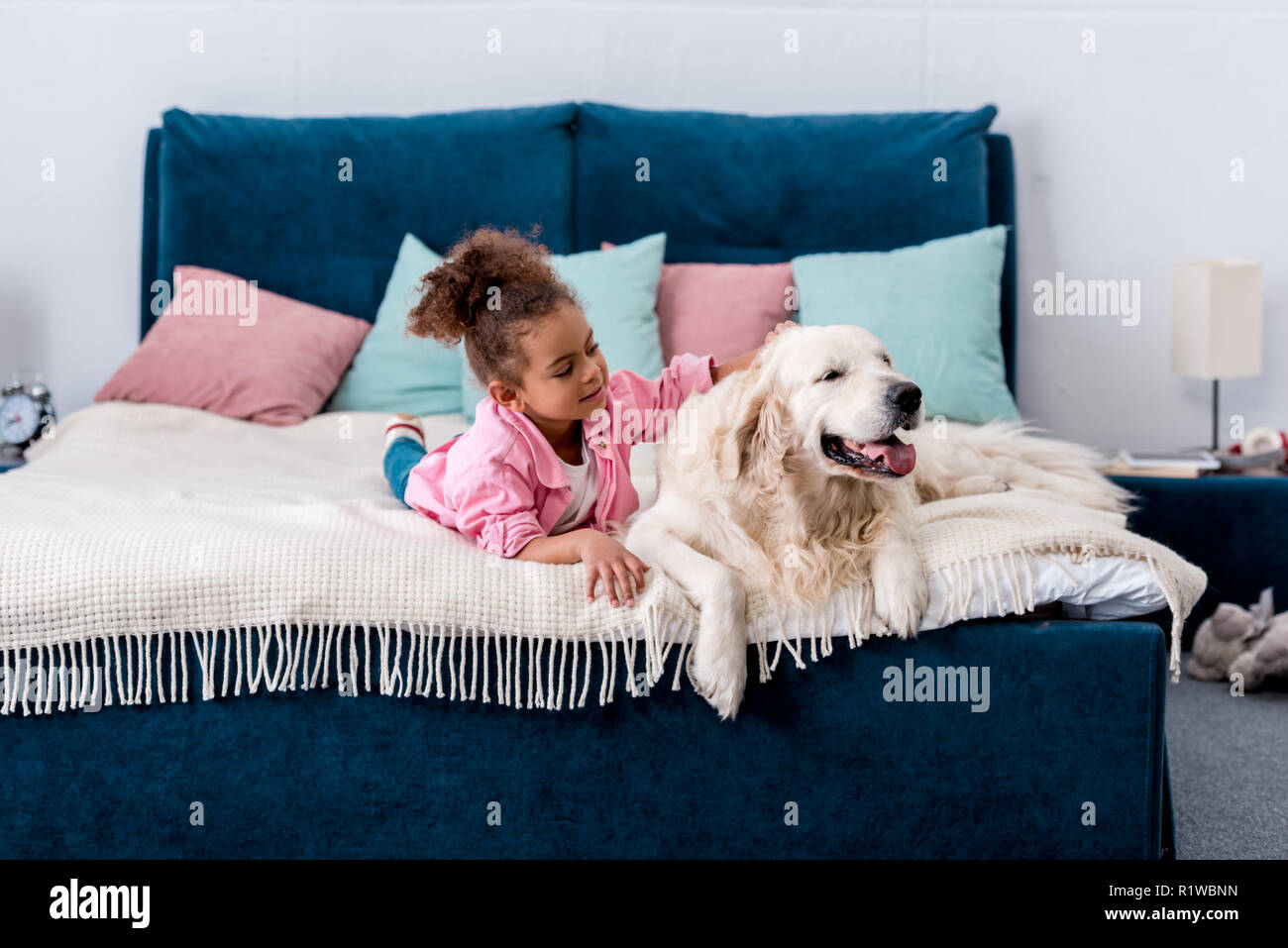 L'Afrique de l'Adorable enfant américain étendu sur le lit et de se gratter le dos d'un chien Banque D'Images