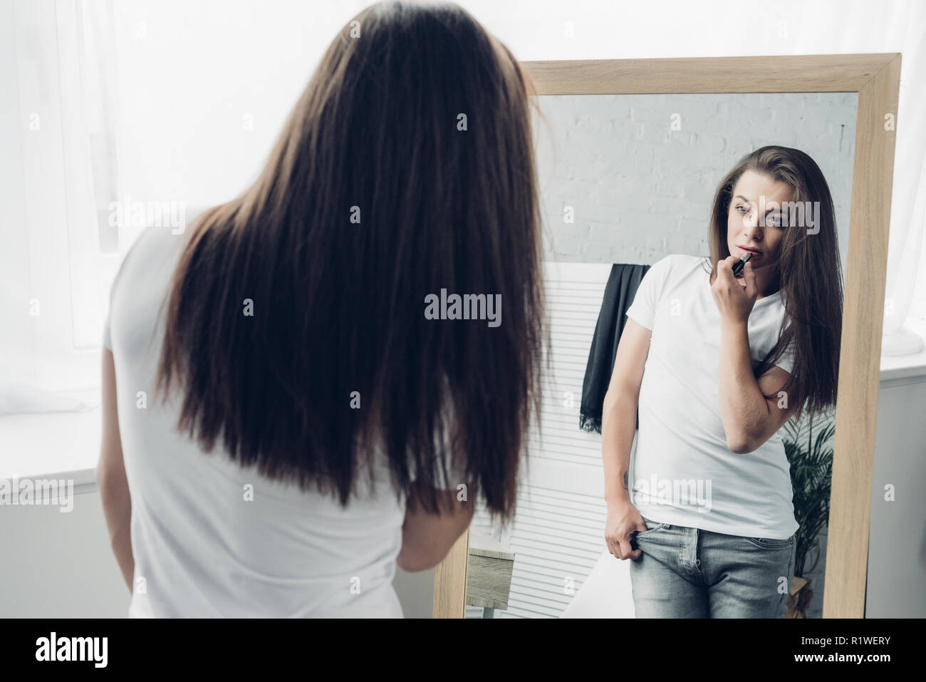 Jeune homme transgenre appliquer le rouge à lèvres tout en regardant mirror Banque D'Images