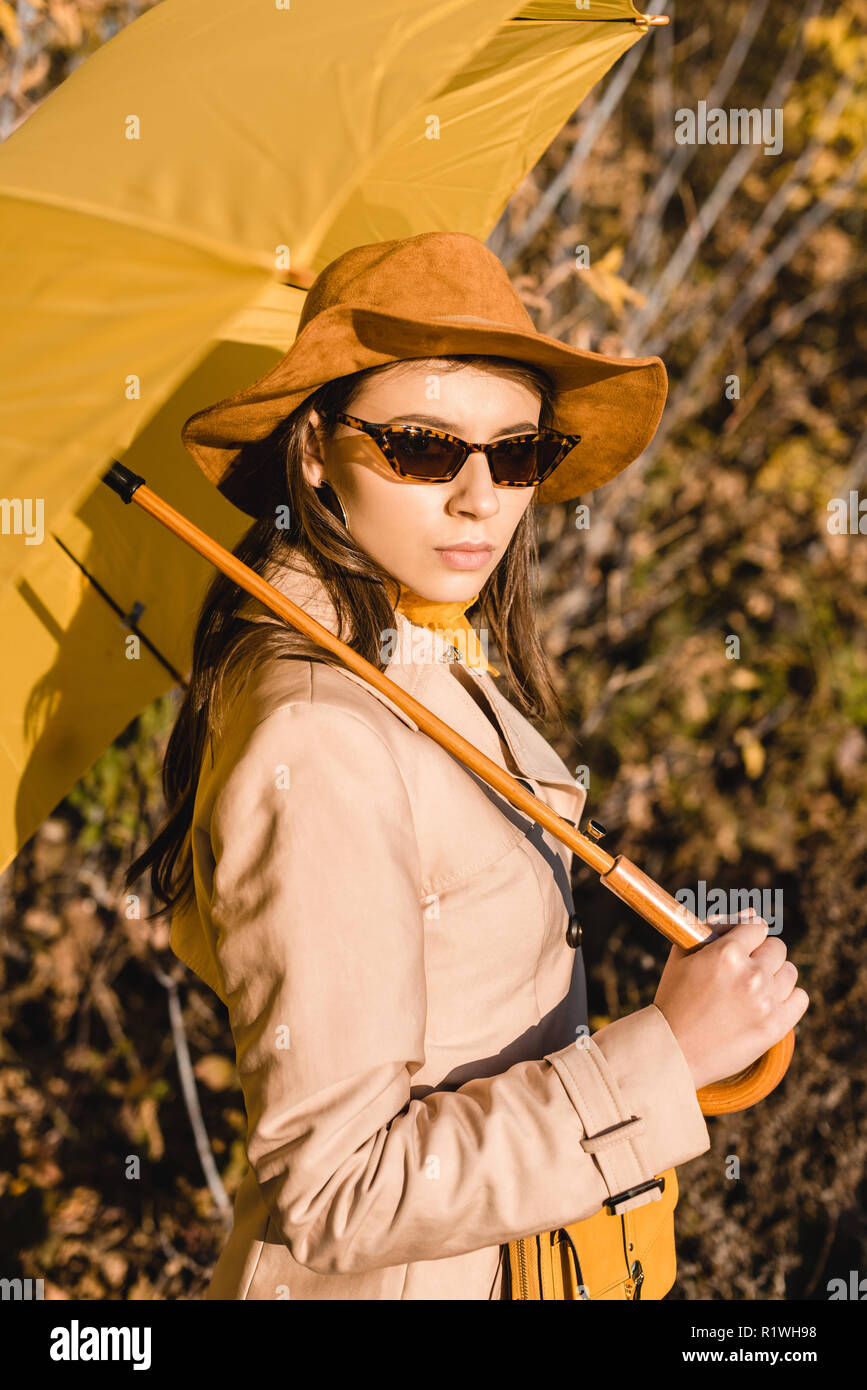 Femme élégante élégante dans des lunettes de soleil et chapeau à la caméra  à l'extérieur et en le parapluie jaune Photo Stock - Alamy