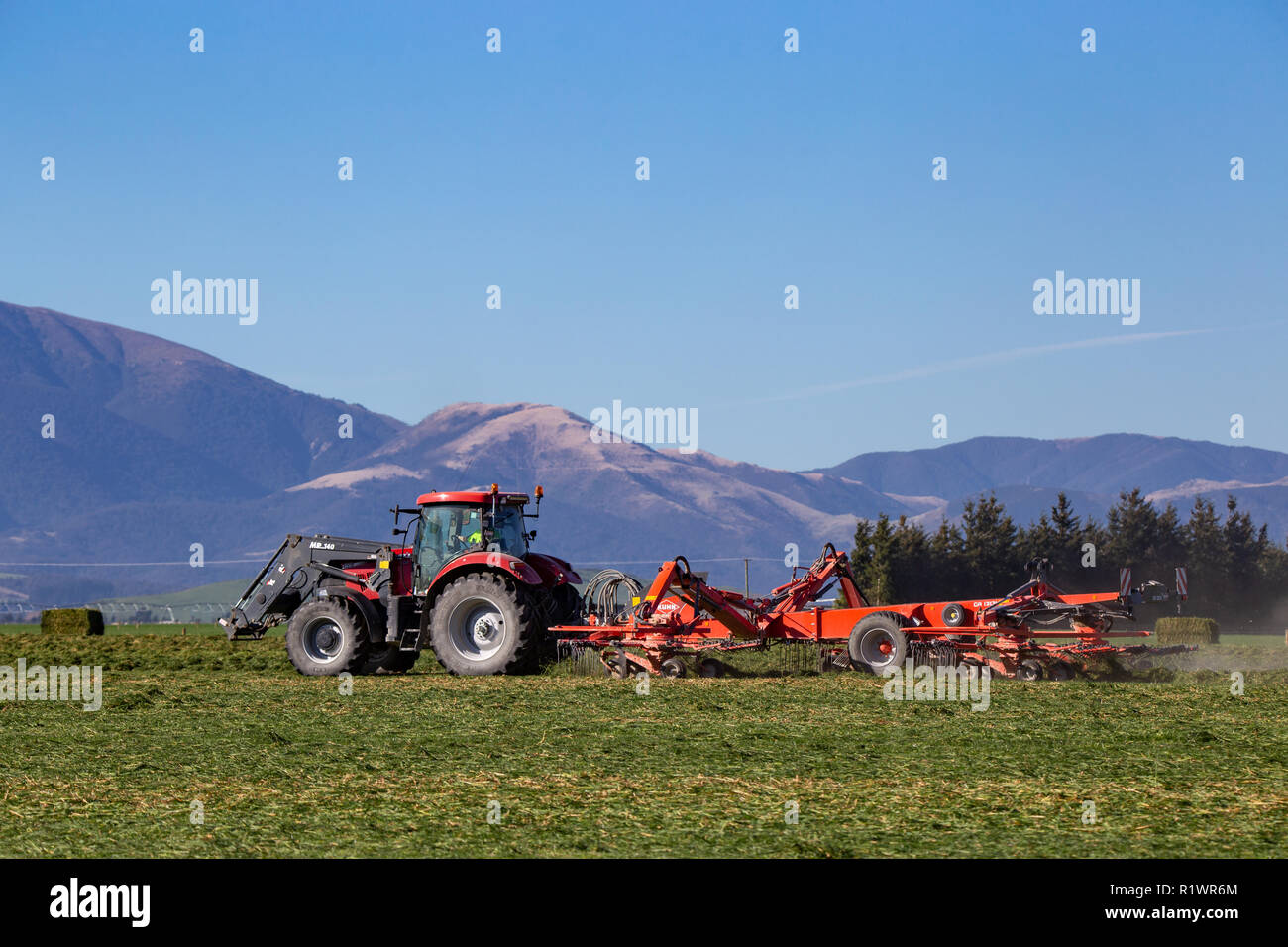 Machines agricoles rouge travaillant dans une zone rurale de la Nouvelle-Zélande la coupe et ratissage des cultures à faire du foin Banque D'Images