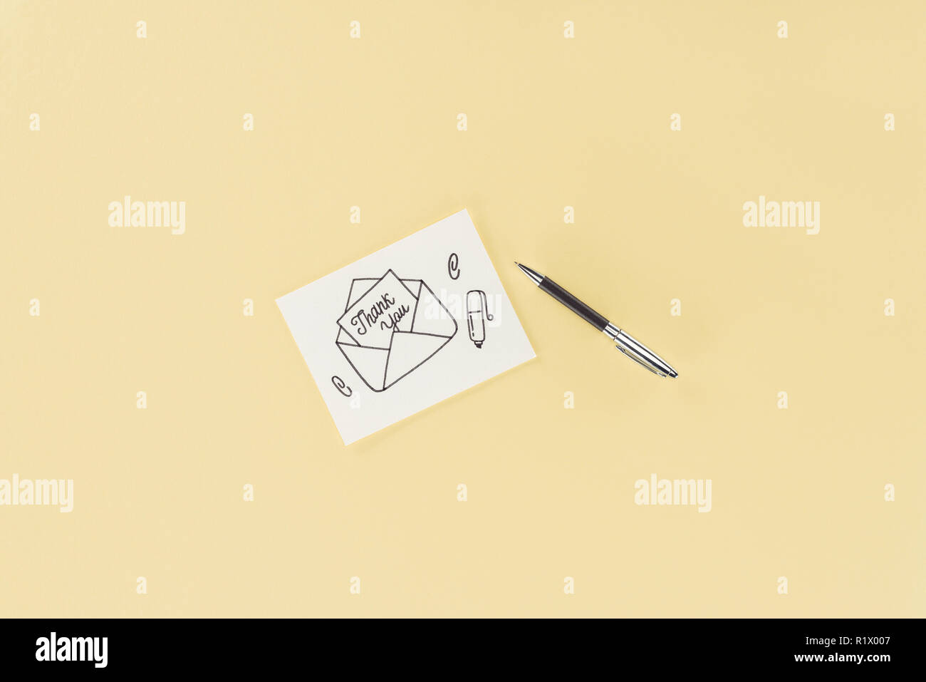 Carte blanche avec lettrage merci sortant de l'enveloppe à la main et un stylo isolé sur fond jaune Banque D'Images