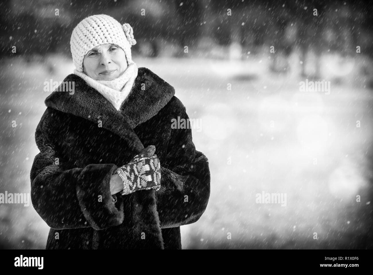 Un hiver portrait of a smiling senior femme portant un chapeau de laine, une écharpe et des gants de couleur, avec un fond de neige Banque D'Images