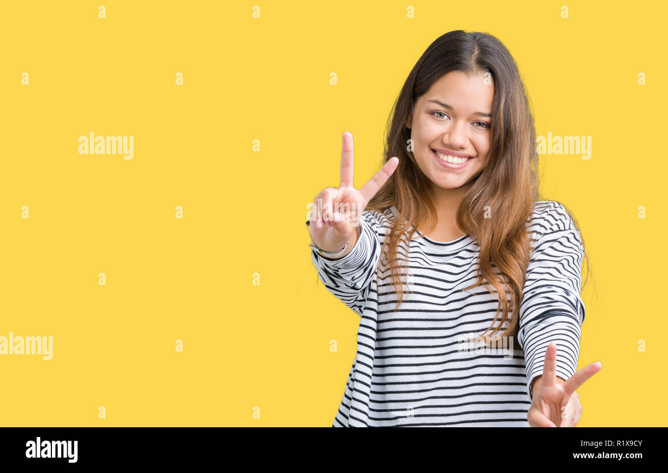 Jeune belle brunette woman wearing sweater à rayures sur fond isolé à sourire à l'appareil photo montrant les doigts faisant signe de victoire. Numb Banque D'Images