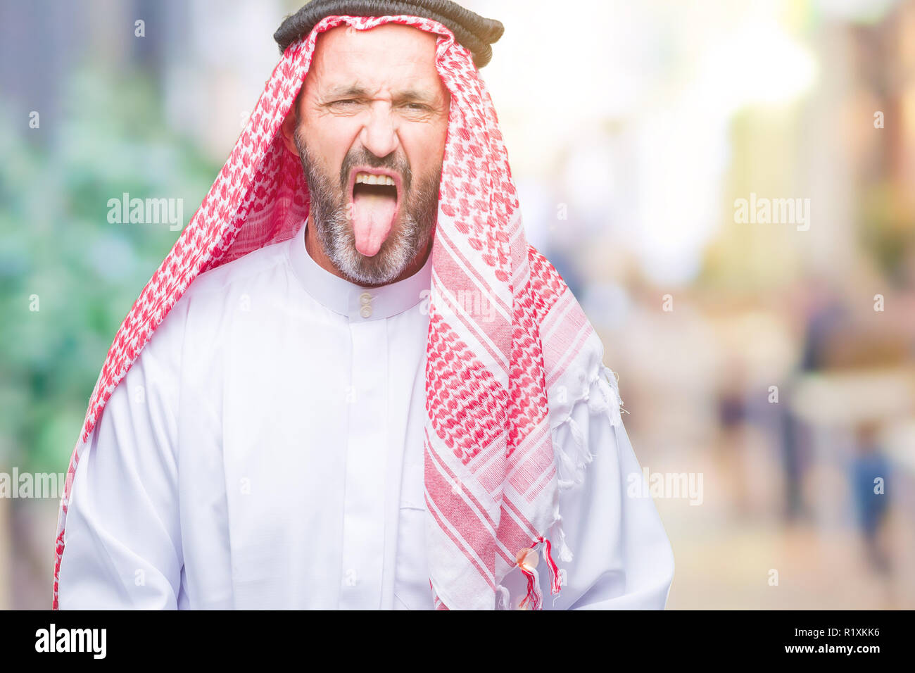 Arabe Senior homme portant un keffieh sur fond isolé sticking tongue out heureux avec drôle d'expression. Concept d'émotion. Banque D'Images