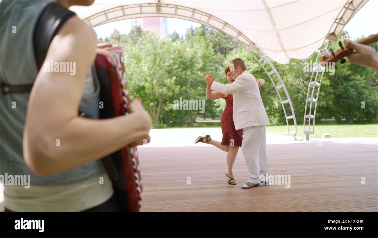 Accordéon et violon jouant dans le parc. Une femme dans une robe rouge et un homme dans un costume blanc sont la danse tango. Un couple de personnes âgées danser le tango dans le parc. Banque D'Images