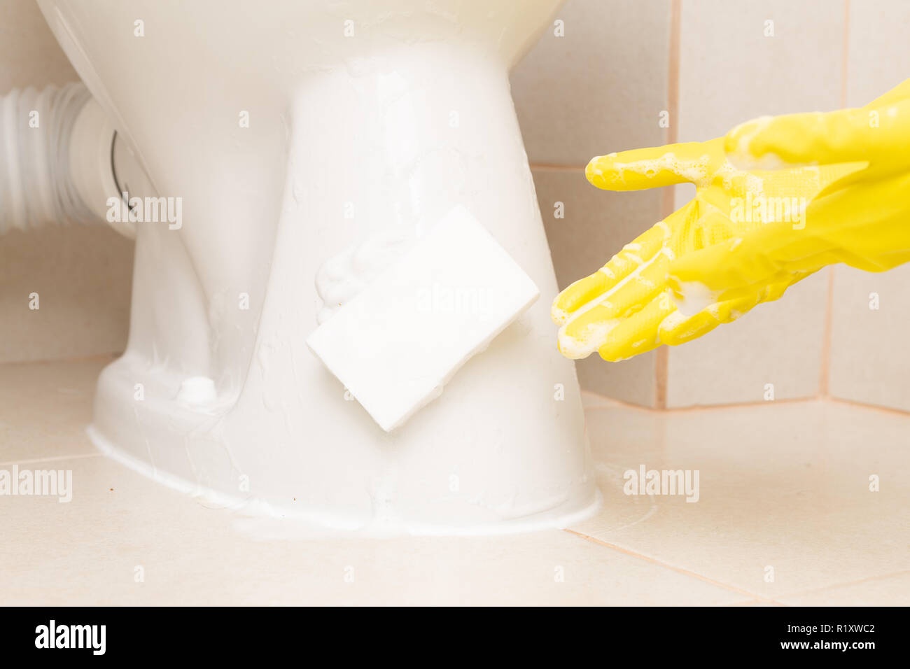 Éponge blanc sur porcelaine toilettes étant présenté avec gant de caoutchouc jaune avec de la mousse Banque D'Images