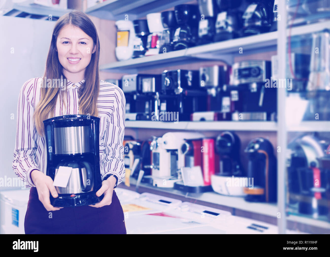 Souriante jeune femme vendeur montrant cafetière dans les appareils domestiques l'article Banque D'Images