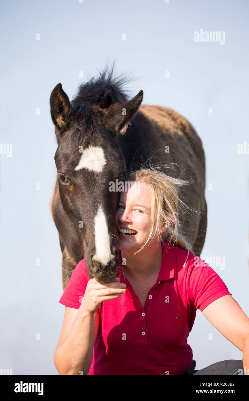 Warmblood. Laughing woman avec poulain ludique sur un pâturage. Allemagne Banque D'Images