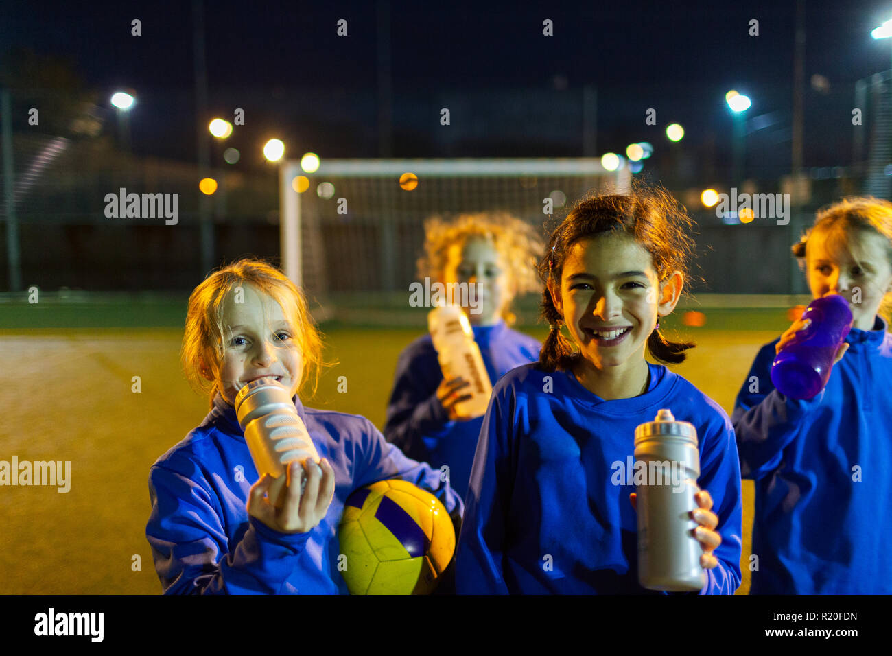 Portrait smiling girls soccer team prenant une pause dans la pratique, l'eau potable sur la nuit sur le terrain Banque D'Images