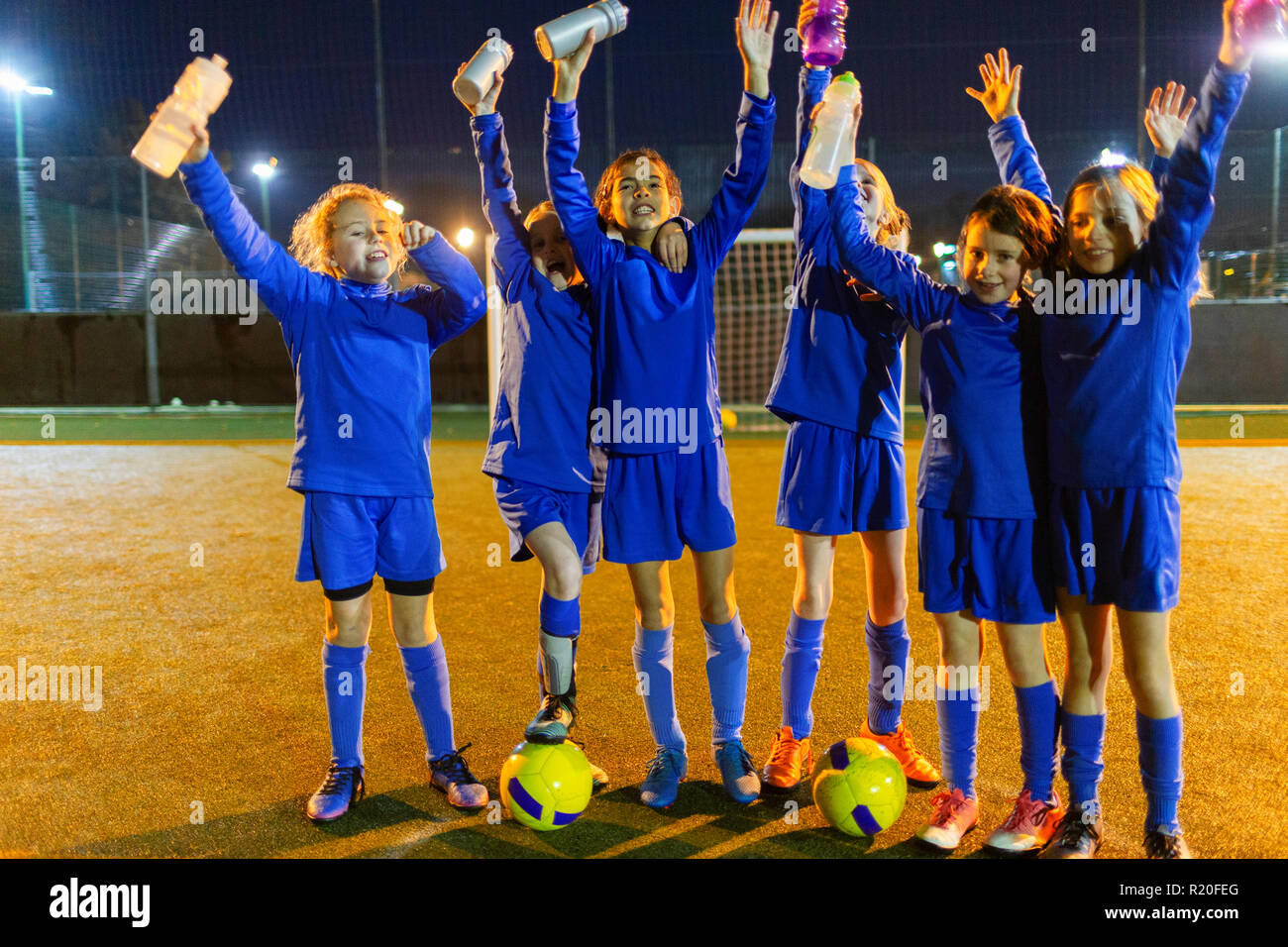 Équipe féminine de soccer Portrait confiant avec des bouteilles d'eau en train d'encourager la nuit sur le terrain Banque D'Images