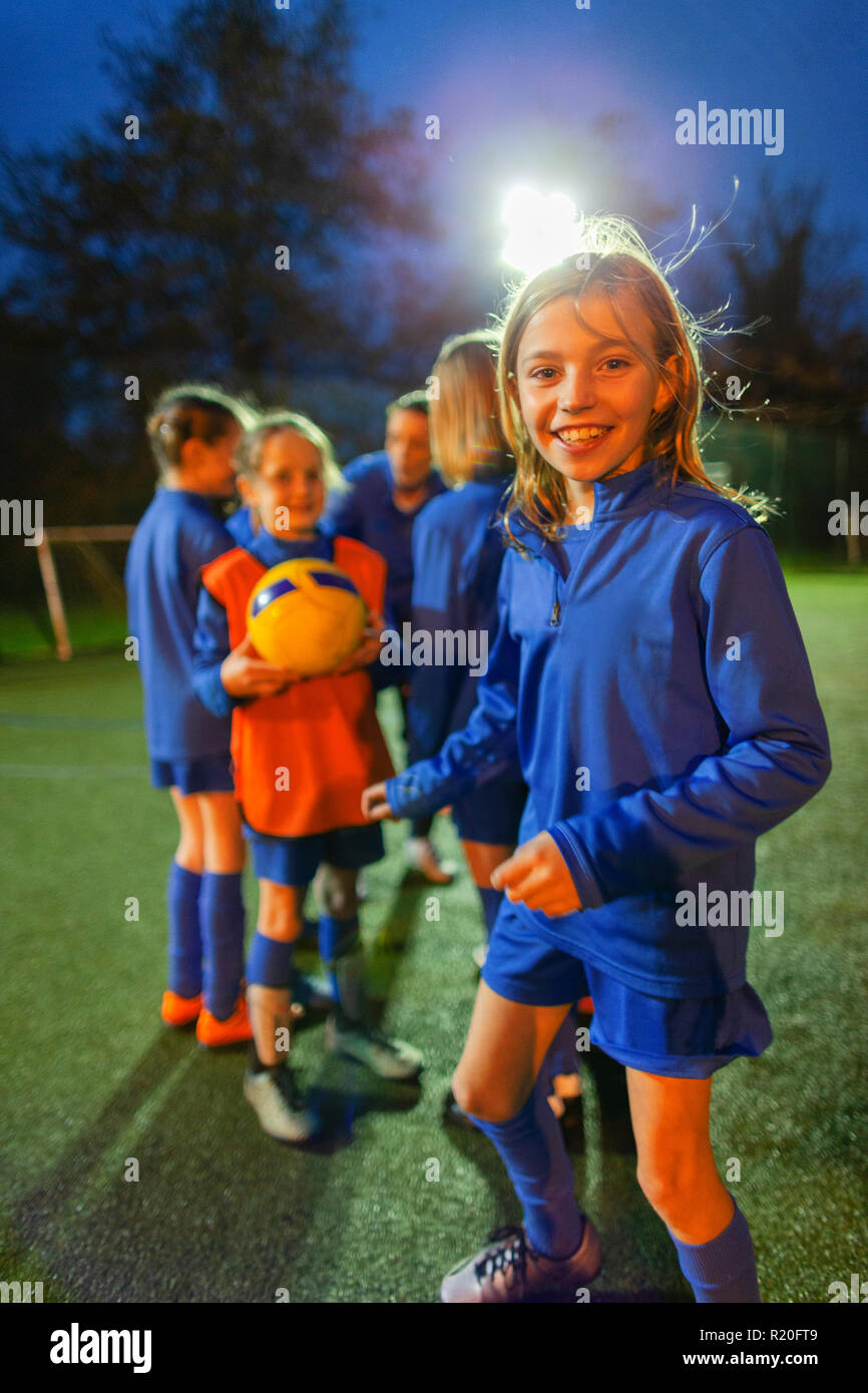 Portrait souriant, confiant girl soccer player pratiquer avec l'équipe de nuit sur le terrain Banque D'Images