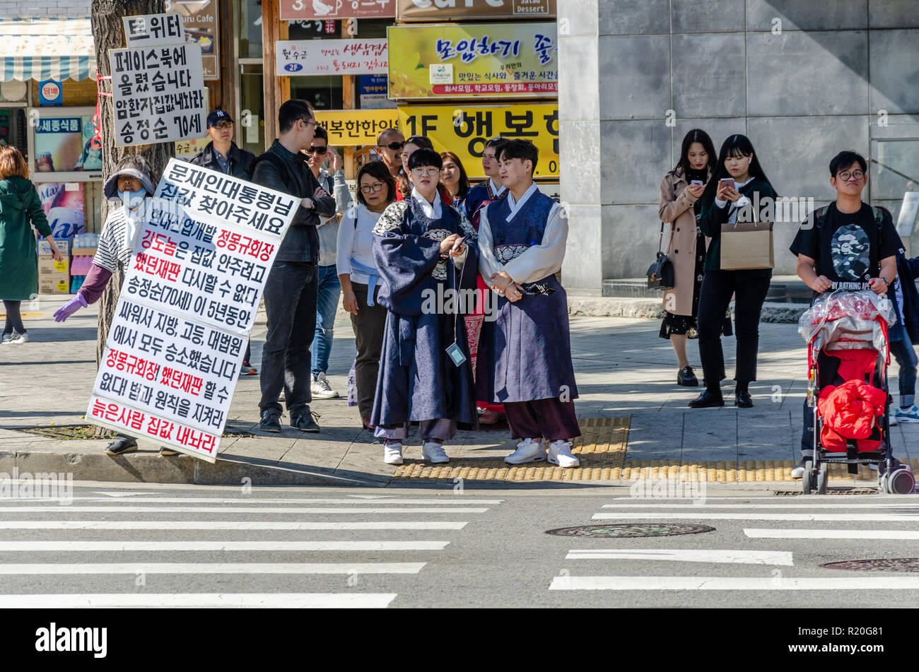 Une personne avec des pancartes organise une manifestation d'un homme en tant que touristes habillés en costume traditionnel coréen attendre pour traverser la route à un passage pour piétons. Banque D'Images