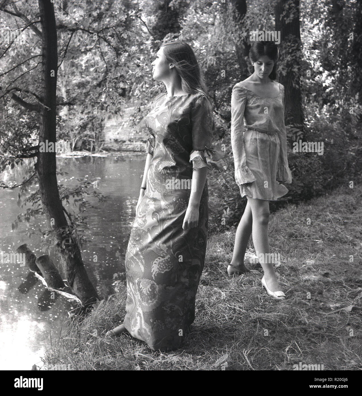1967, deux jeunes filles attracive porter des robes à motifs floral court et à un défilé de tirer par un lac dans une forêt, England, UK. Ce style bohème hippie ou est devenu populaire à la fin des années 60 que la culture des jeunes a commencé à embrasser 'flower power' et musique psychédélique. Banque D'Images