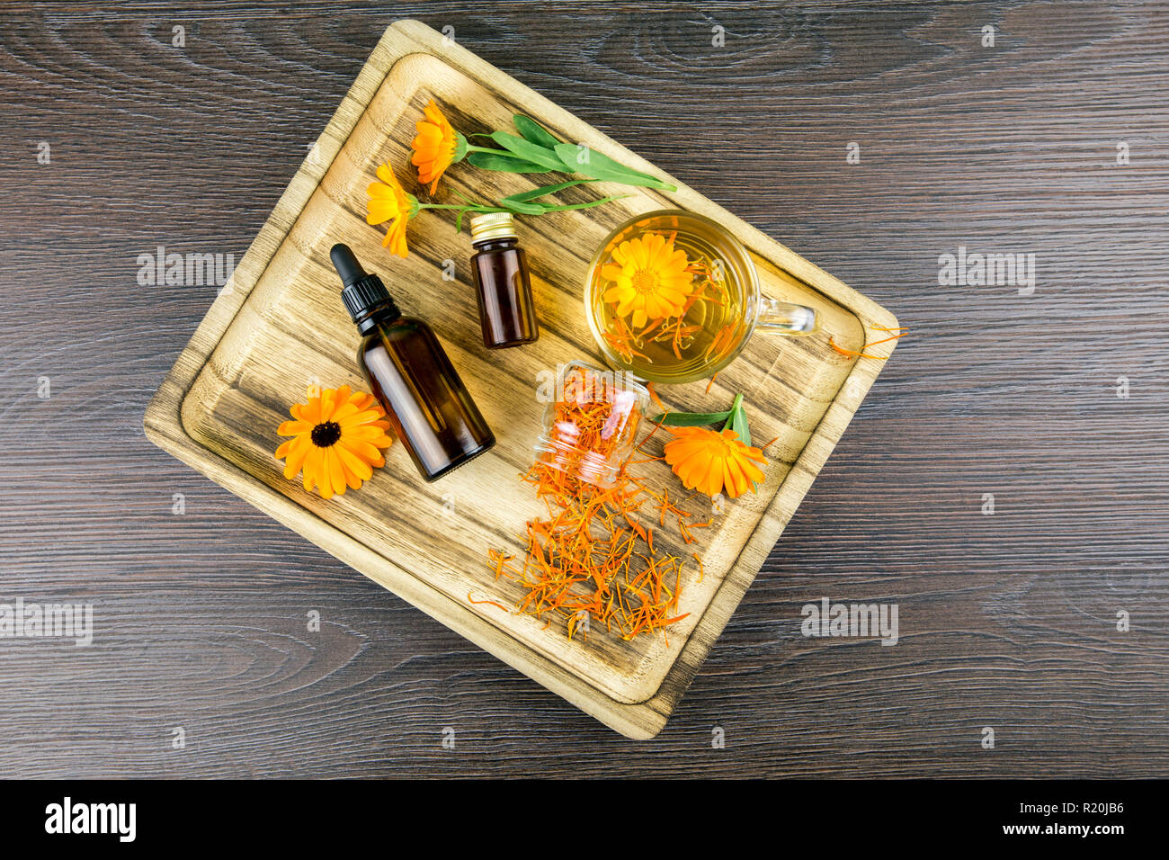 Calendula officinalis, le souci officinal, ruddles, marigold commun ou Scotch marigold différents produits de santé sur le plateau en bois, huile essentielle, teinture Banque D'Images