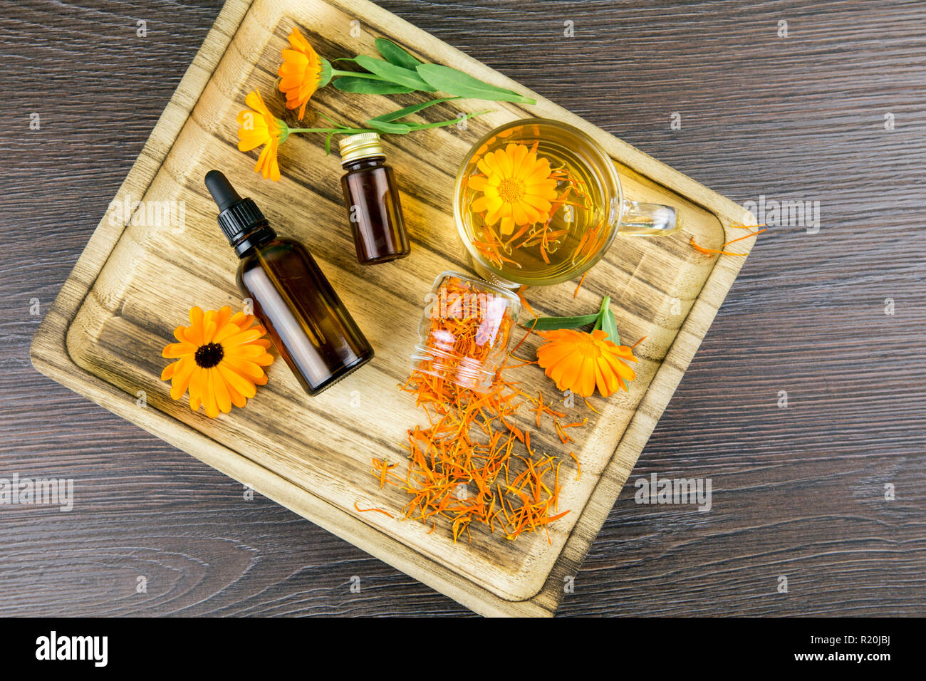 Calendula officinalis, le souci officinal, ruddles, marigold commun ou Scotch marigold différents produits de santé sur le plateau en bois, huile essentielle, teinture Banque D'Images