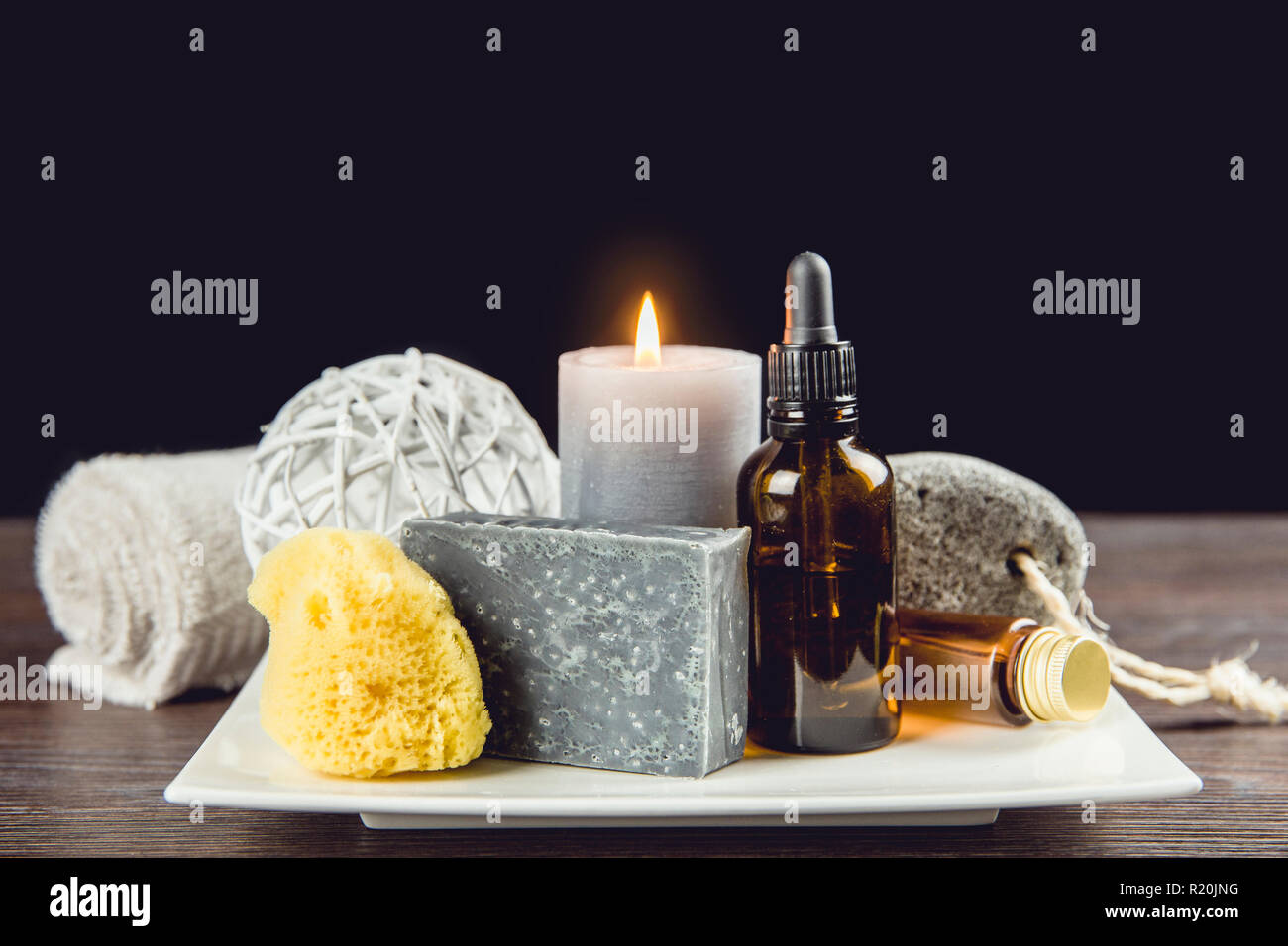 Homme spa relaxation concept. Spa de jour différents produits sur le plateau en céramique blanche sur table en bois foncé, fond noir. Banque D'Images