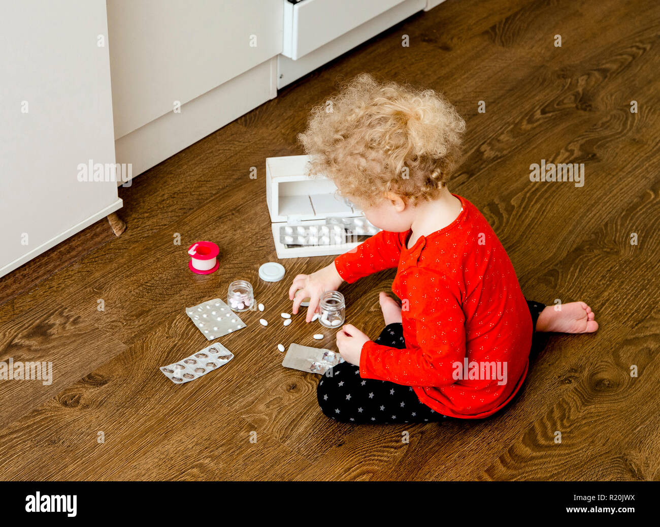 Jeune enfant jouer seul avec des comprimés comprimés sur accueil plancher de la cuisine. Conserver à l'écart des enfants à atteindre concept. Pas d'armoire à pharmacie. Banque D'Images