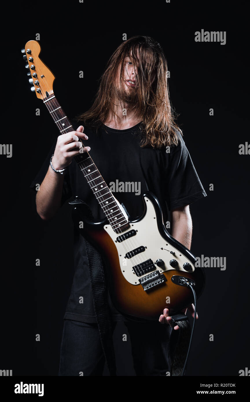 Studio portrait : un beau jeune homme aux cheveux longs (musicien de rock) est titulaire d'une guitare électrique dans les mains Banque D'Images