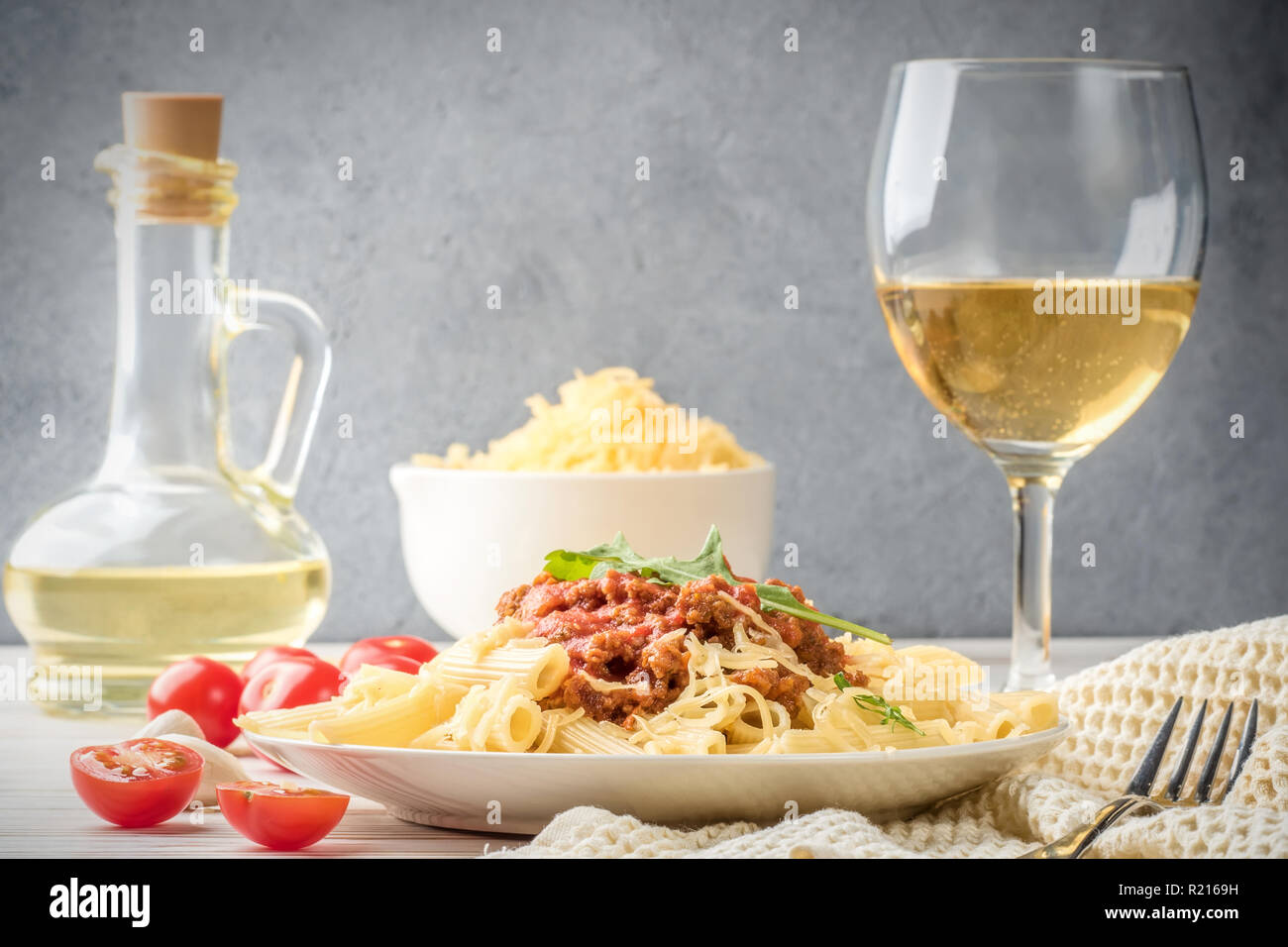 Les pâtes italiennes Penne bolognaise rigatone la viande hachée à la sauce tomate et de parmesan. Nature morte sur table en bois blanc, servi avec des tomates cerises, carafe d'huile d'olive et le verre de vin blanc Banque D'Images