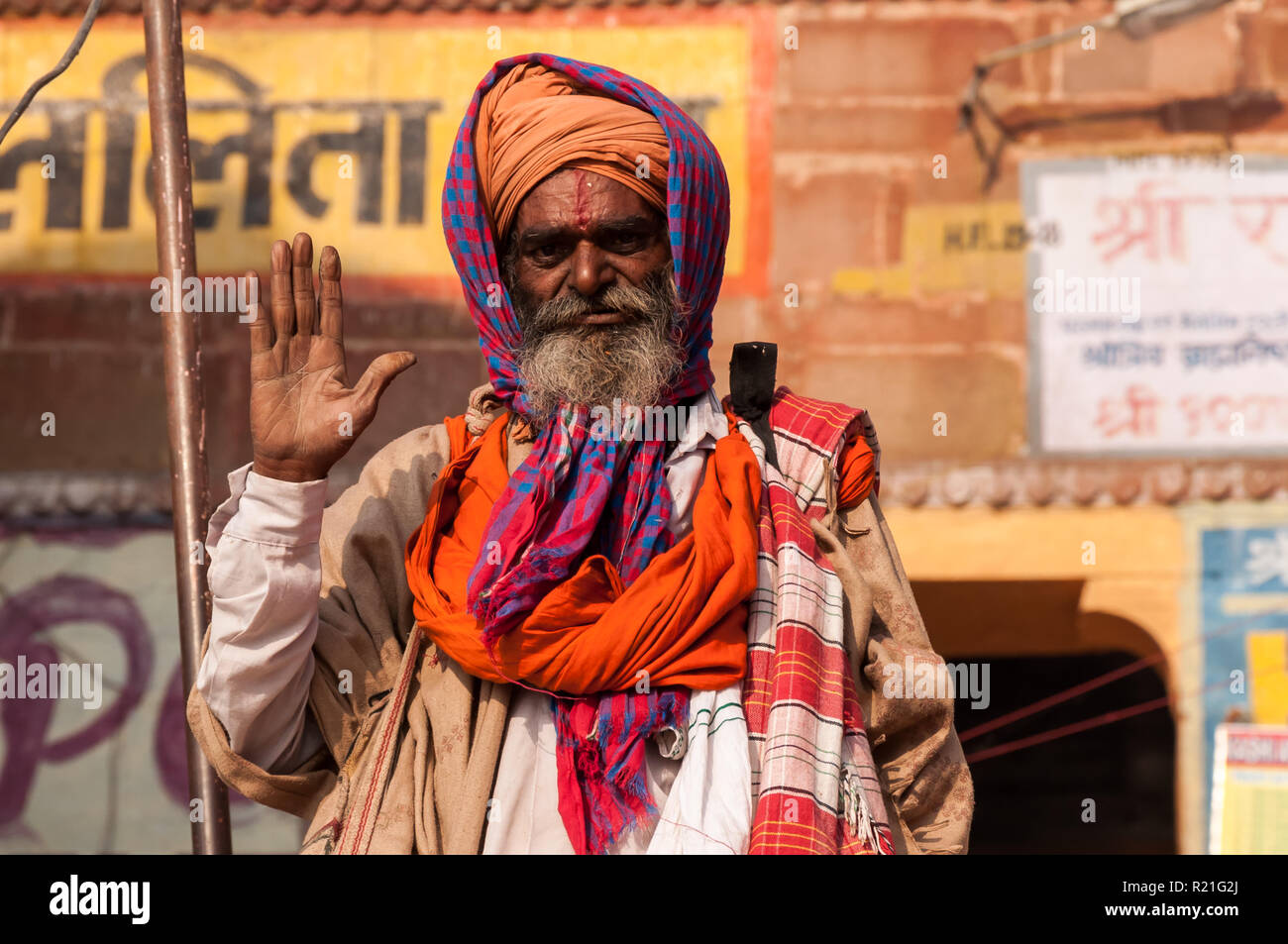 Un sadhu errant avec une main ouverte dans un geste d'amitié contre le fond des inscriptions hindoues sur le mur. Inde Varanasi 2012 Banque D'Images