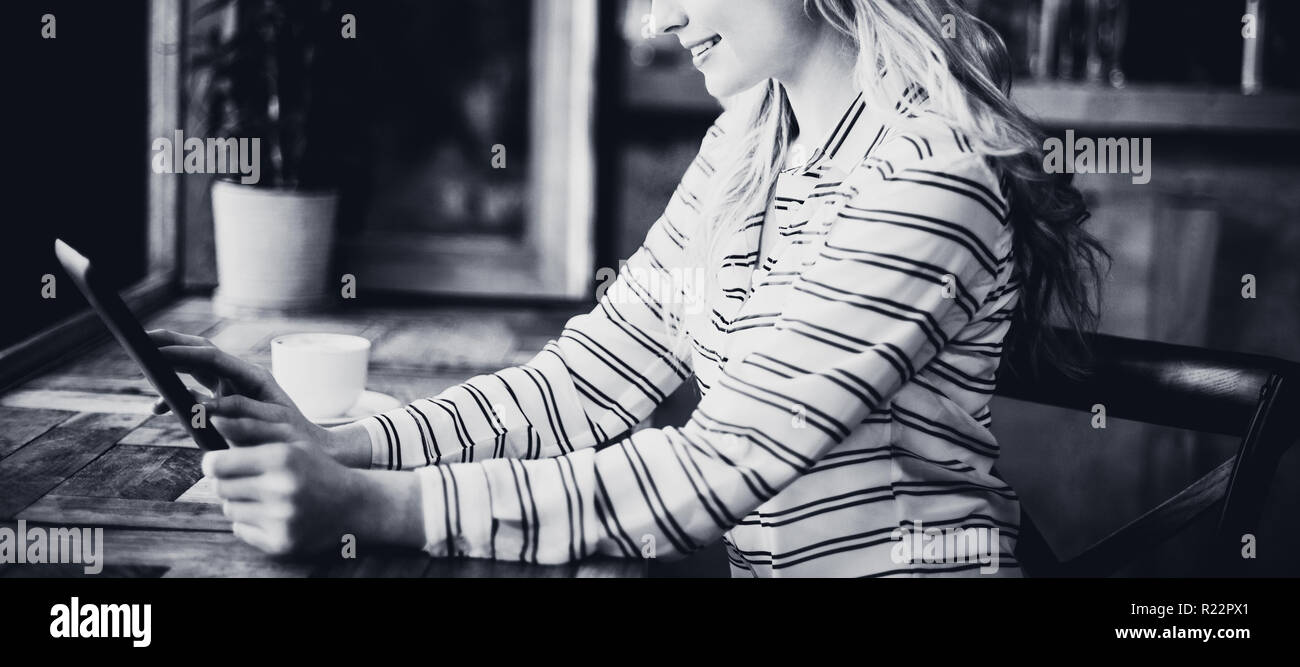 Smiling woman using digital tablet while having coffee Banque D'Images