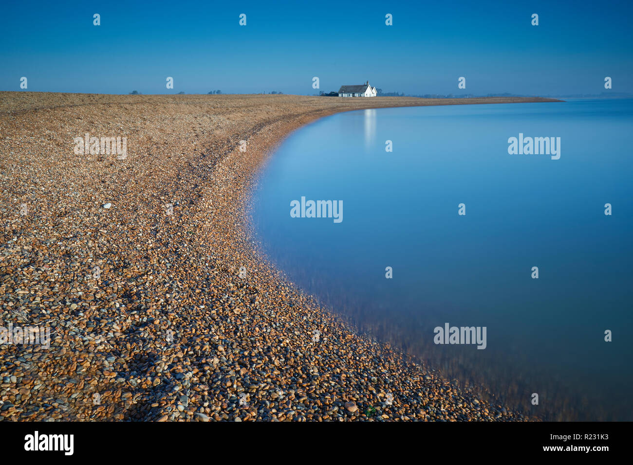 La plage incurvée à Shingle Street et d'un cottage blanc au loin avec la mer bleue et ciel bleu clair sur un jour d'automne, Suffolk, Angleterre, RU Banque D'Images