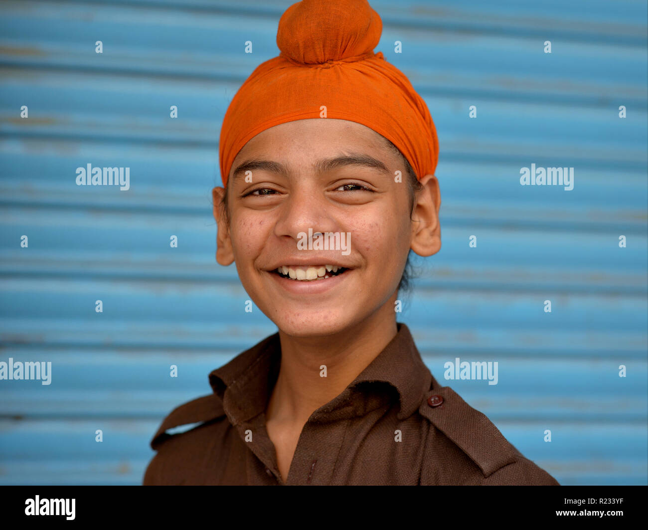 Sikh indien teen boy porte un sourire orange patka et pour l'appareil photo. Banque D'Images