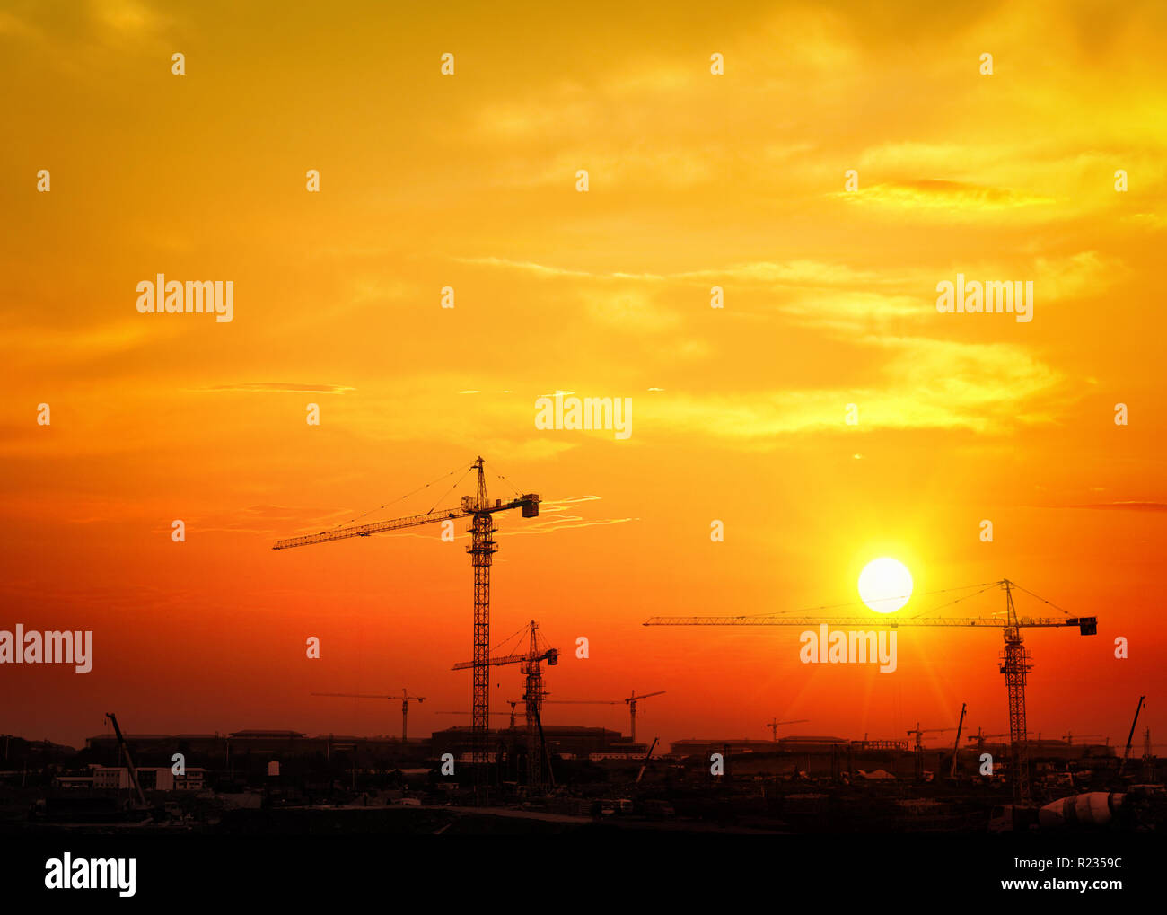 Grues de construction industrielle et de la construction de plus de silhouettes de soleil au lever du soleil. Banque D'Images