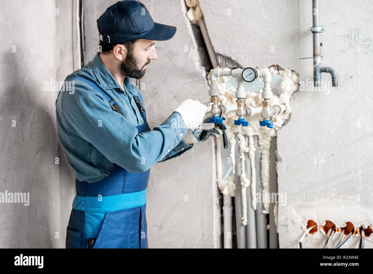 Workman en uniforme bleu de l'installation de chauffage de l'eau sur le site de construction d'une maison neuve. Banque D'Images