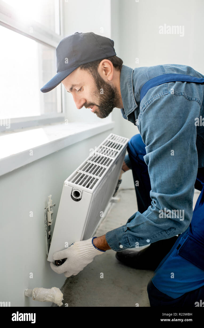 Montage du radiateur de chauffage de l'eau ouvrier près de la fenêtre dans le salon rénové blanc Banque D'Images