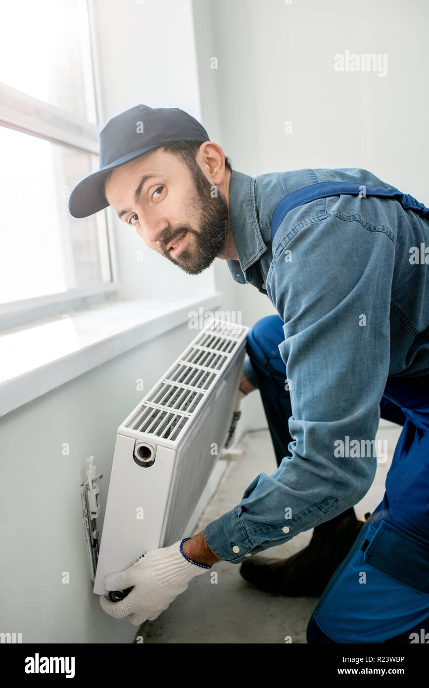 Portrait d'un ouvrier de l'eau fixation du radiateur de chauffage près de la fenêtre dans le salon rénové blanc Banque D'Images