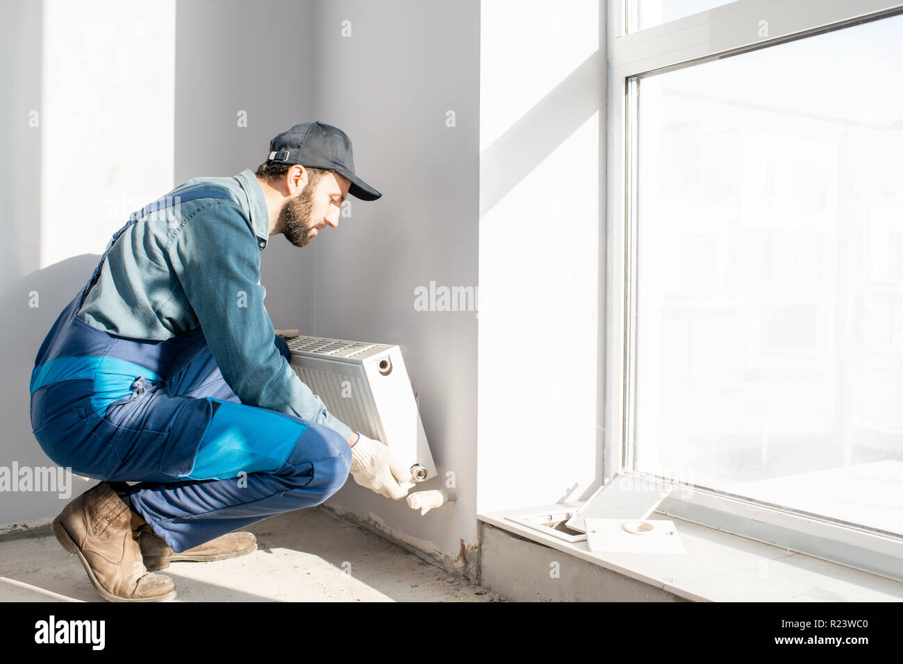 Montage du radiateur de chauffage de l'eau ouvrier près de la fenêtre dans le salon rénové blanc, Image with copy space Banque D'Images
