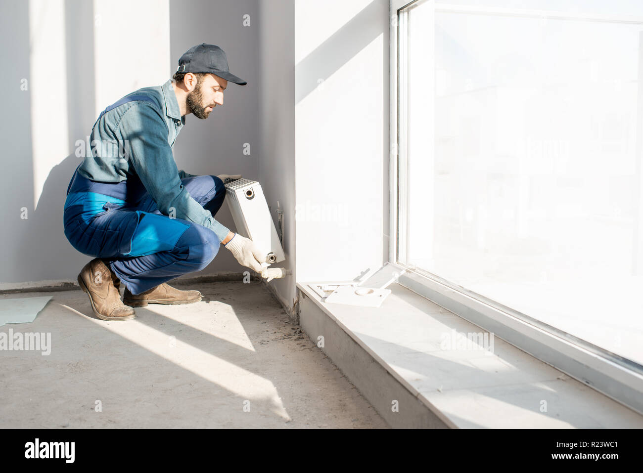Montage du radiateur de chauffage de l'eau ouvrier près de la fenêtre dans le salon rénové blanc, Image with copy space Banque D'Images