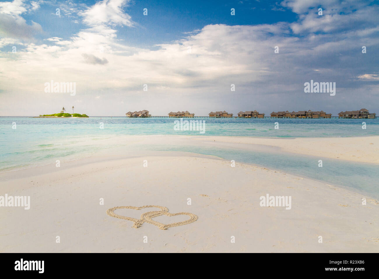 Deux coeurs tirés sur le sable d'une plage tropicale au coucher du soleil. Océan turquoise clair. Maldives îles au-dessus des villas et des bungalows d'eau. Voyage romantique Banque D'Images