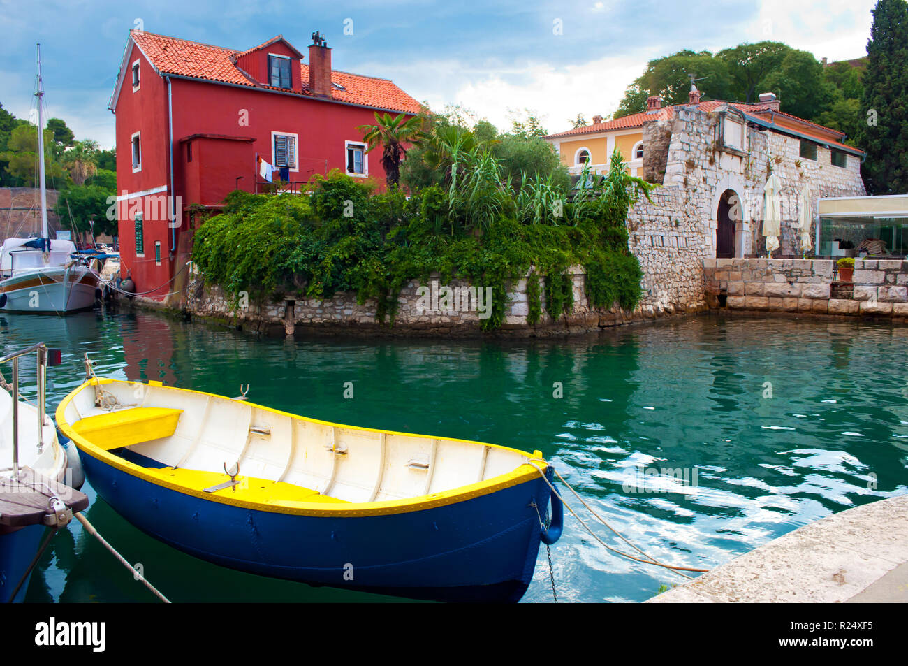 Ambiance pittoresque ville de Zadar, Croatie. Maison Rouge parmi le feuillage lierre vert près de l'eau émeraude où un bateau bleu et jaune et plusieurs bateaux sont fl Banque D'Images