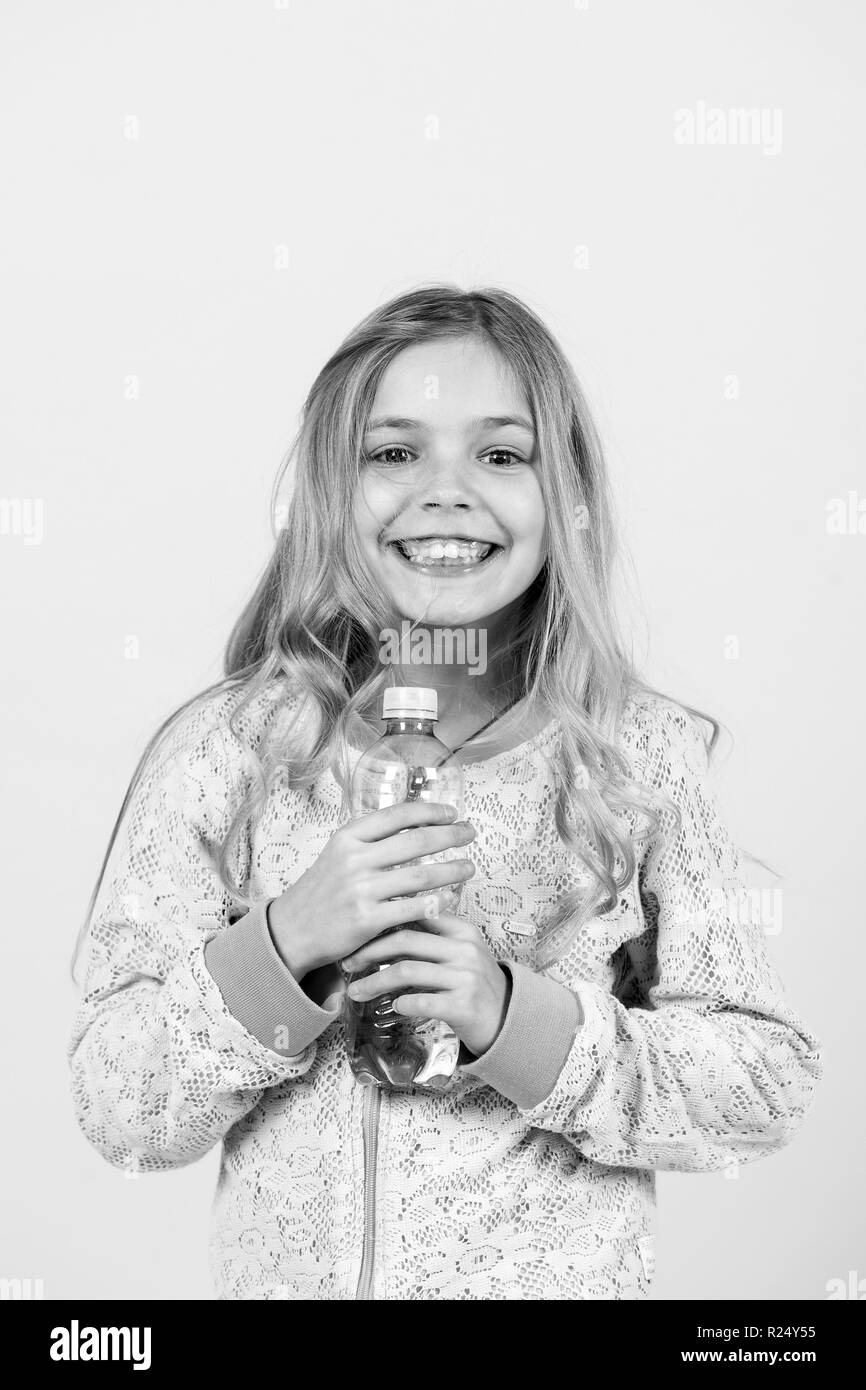 Sourire petite fille avec de l'eau bouteille sur fond orange. Heureux l'enfant avec l'eau potable. Boire de l'eau saine. Source de vie concept. La Nutrition, santé, vie, punchy pastel. Banque D'Images