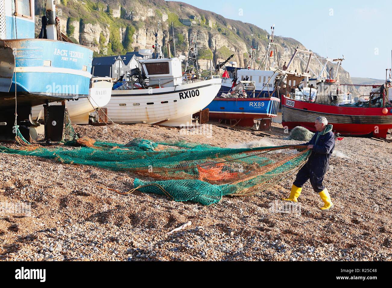 Bateaux de pêche, le stade, plage de pêche historique. Un pêcheur rassemble ses filets de pêche devant les bateaux de pêche sur la seule plage lancée flotte de pêche au royaume-uni après une matinée en mer. Hastings, East Sussex, royaume-uni Banque D'Images