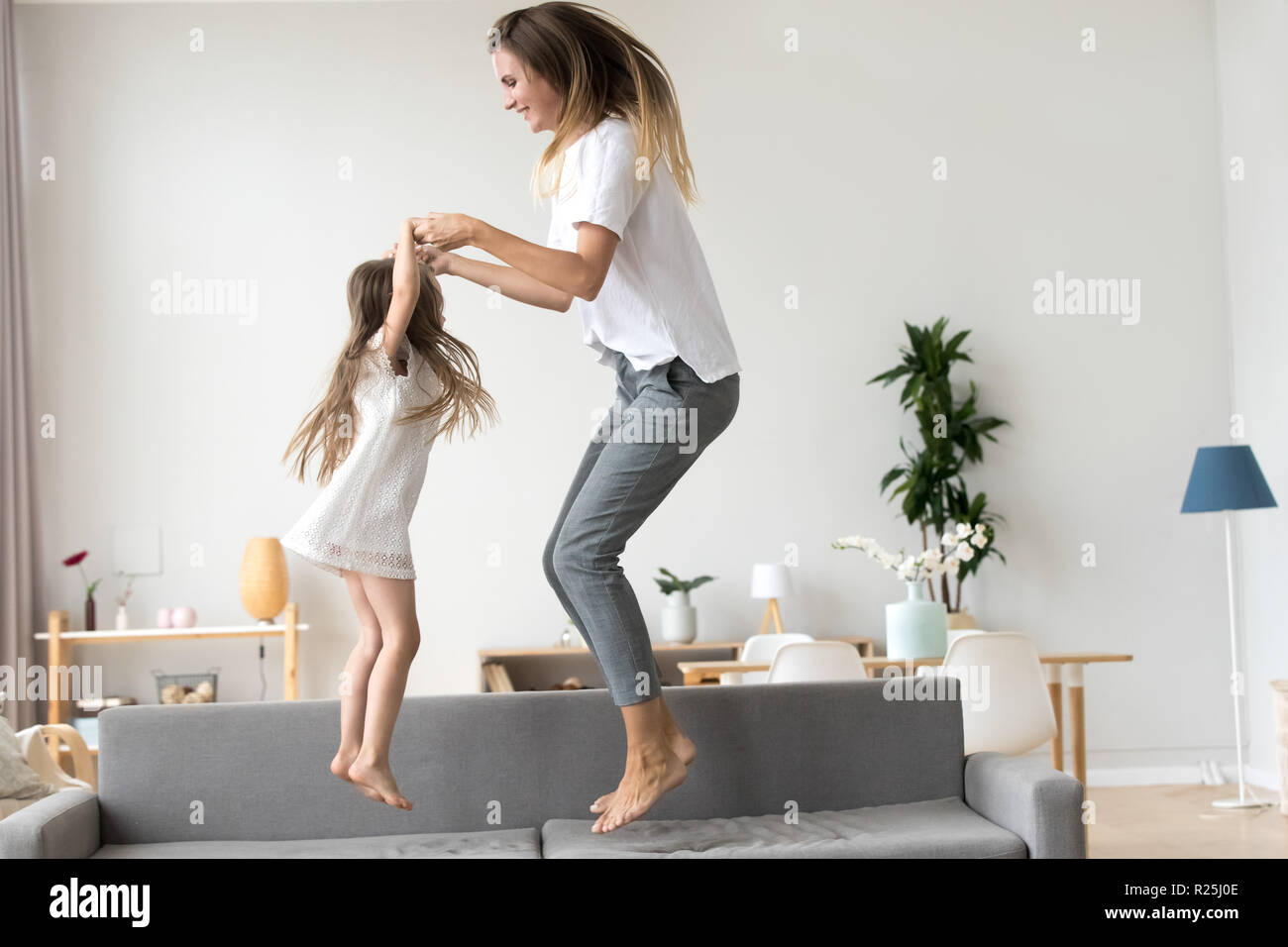 Heureuse maman et enfant fille tenant la main de sauter sur canapé Banque D'Images