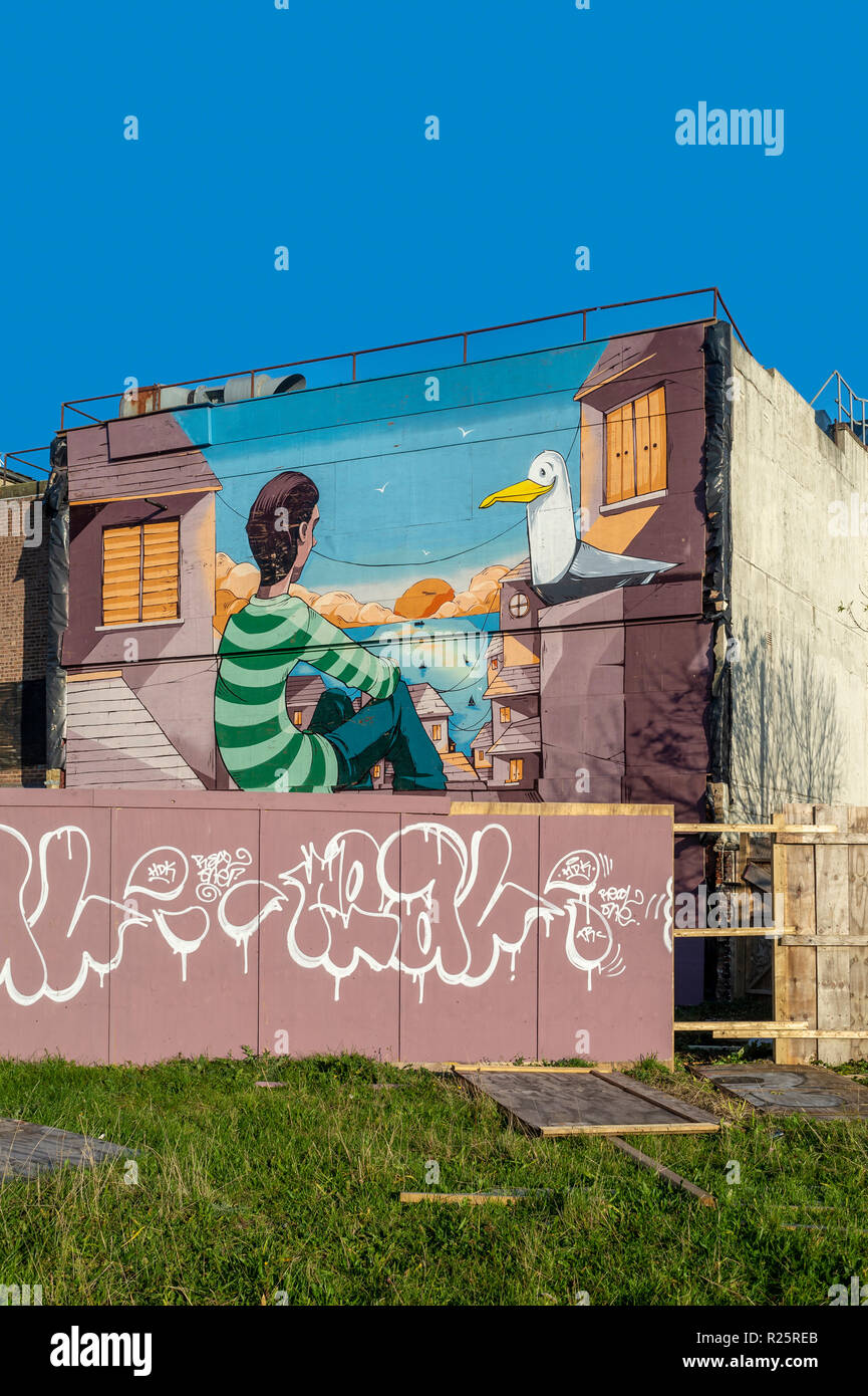 Street art mural peint sur le côté d'un immeuble, l'homme avec une mouette face à la mer. Banque D'Images