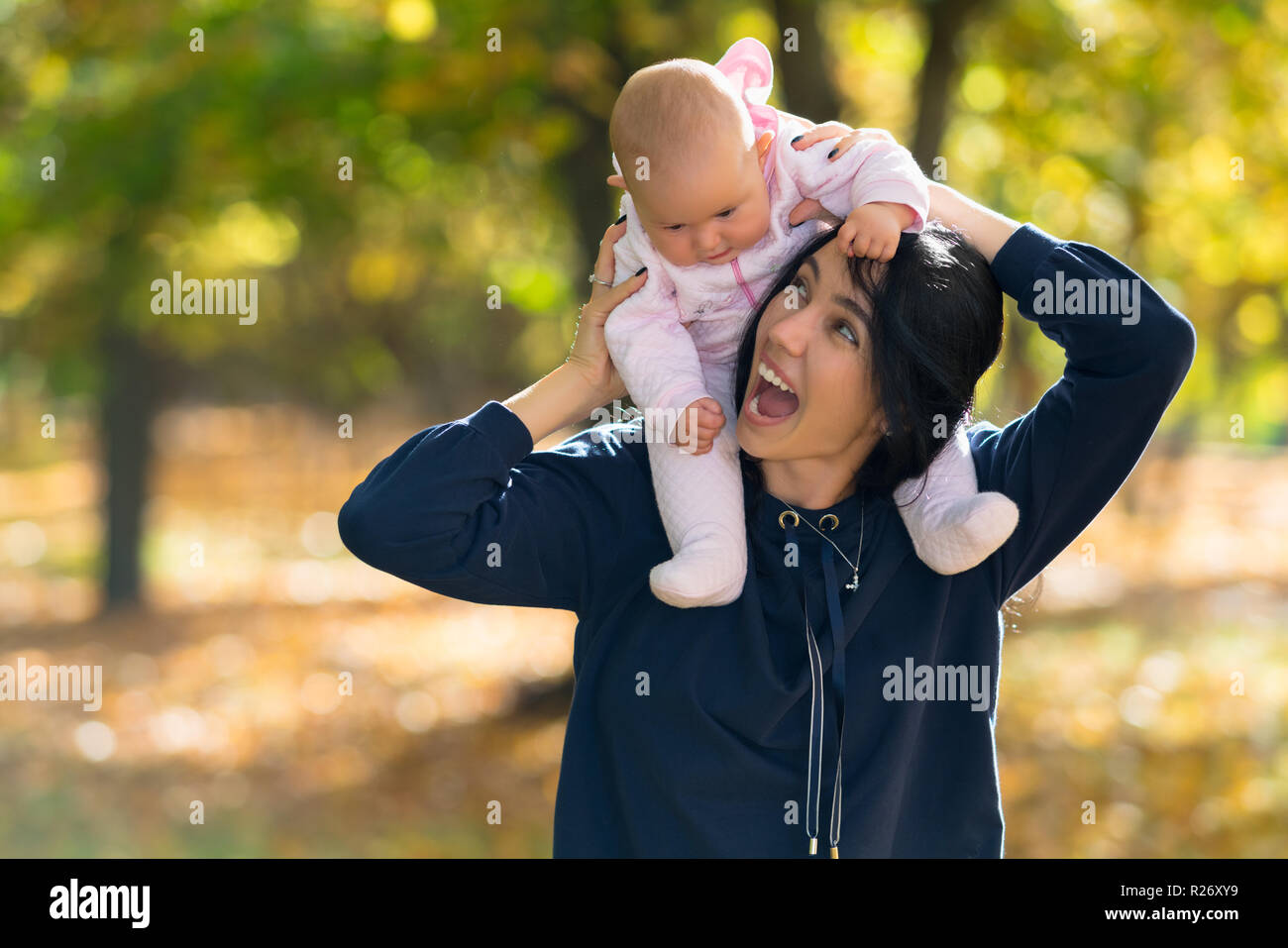 Rire mère donnant son bébé fille un piggy back ride comme ils marchent ensemble à travers une forêt d'automne Banque D'Images