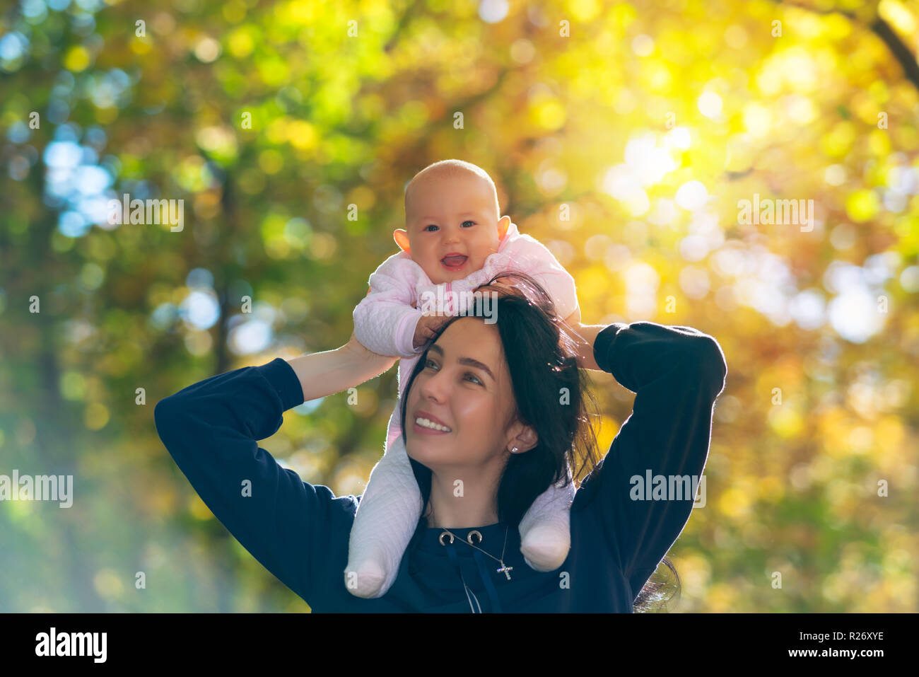 Rire vive little baby girl enjoying a piggy back ride sur les épaules de sa mère dans une forêt d'automne Banque D'Images