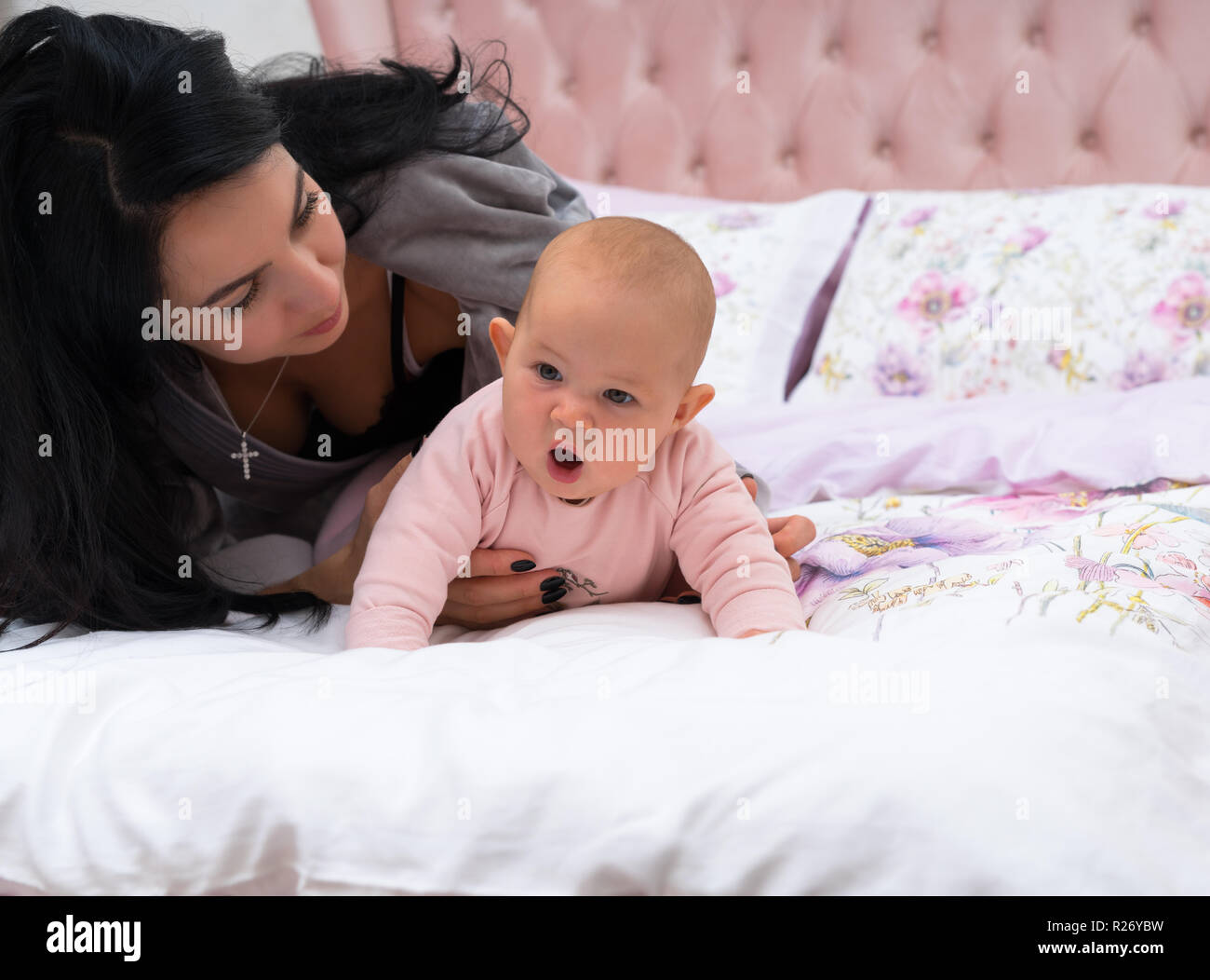 Jeune Mere Aux Cheveux Noirs La Pose A Cote De Son Petit Bebe Tandis Que La Jeune Fille Tente De Se Trainer Au Lit Avec Drole De Visage Vue De Face Avec